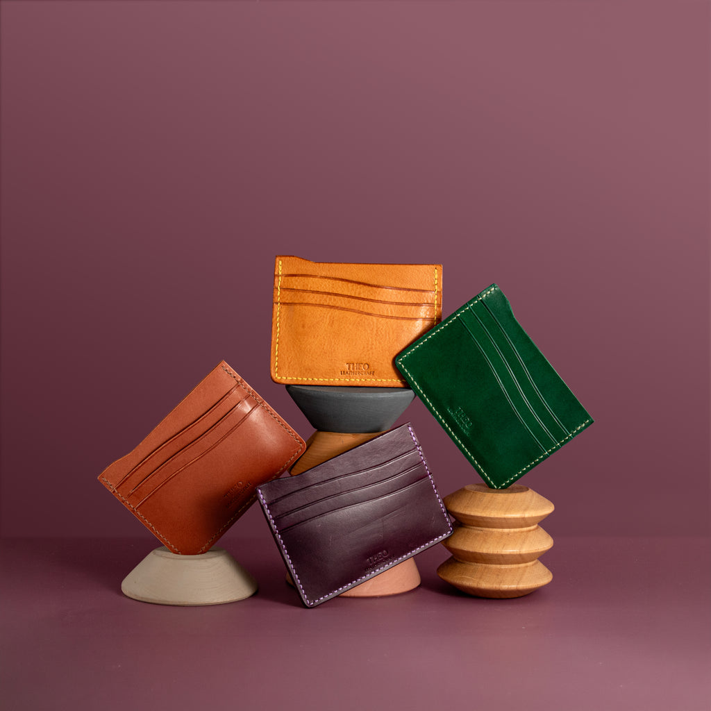 Collection of leather wallets in various colors on a wooden and ceramic stand against a purple background