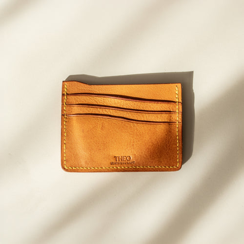 Mustard leather cardholder with 'THEO' branding on a beige background