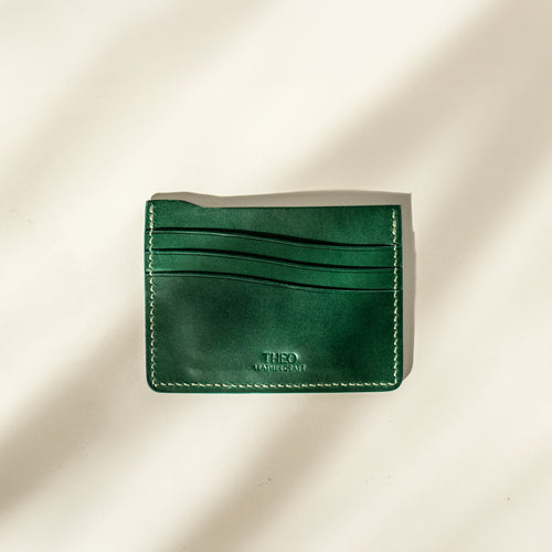 Green leather cardholder with visible branding on a beige background