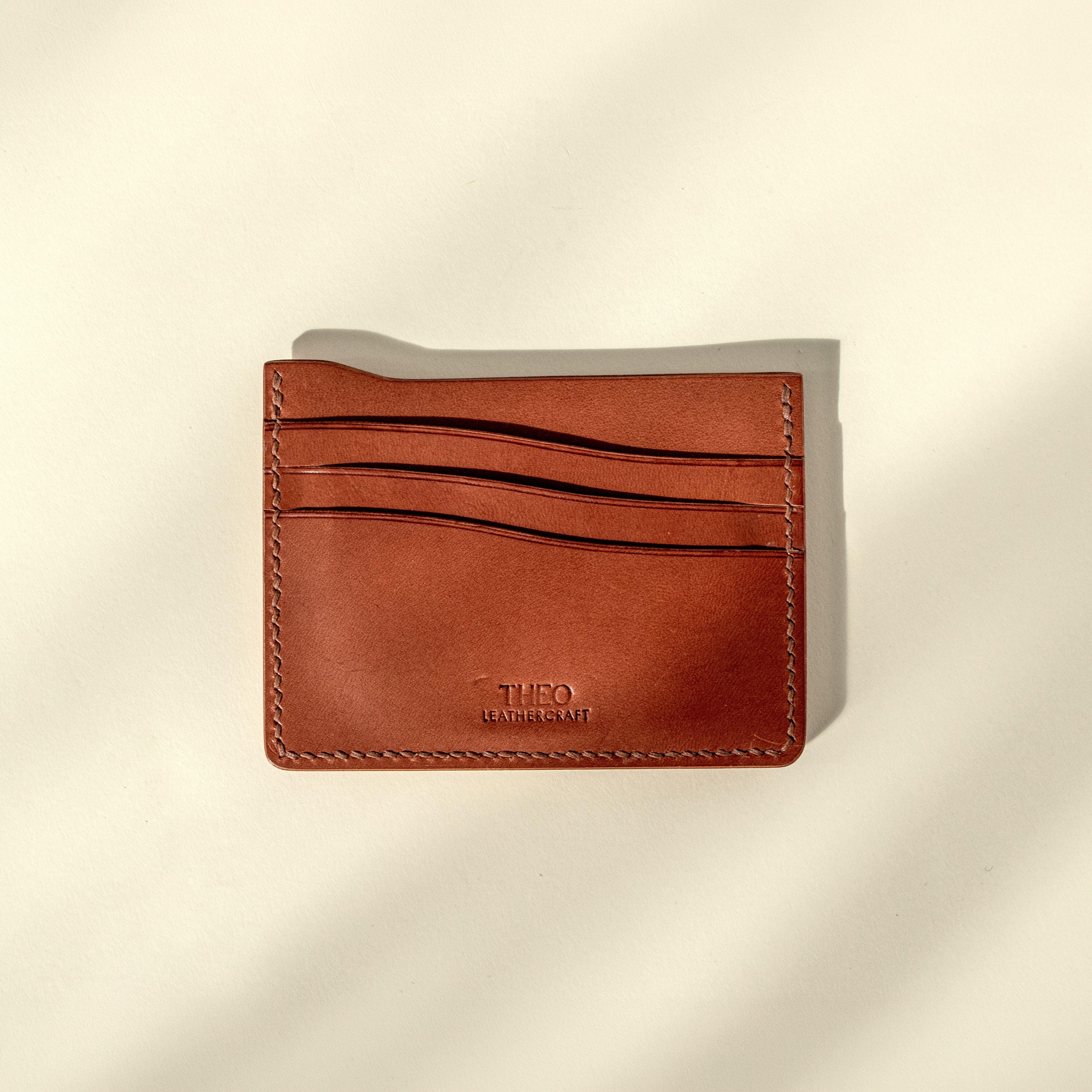 Brown leather cardholder with 'THEO' branding on a beige background